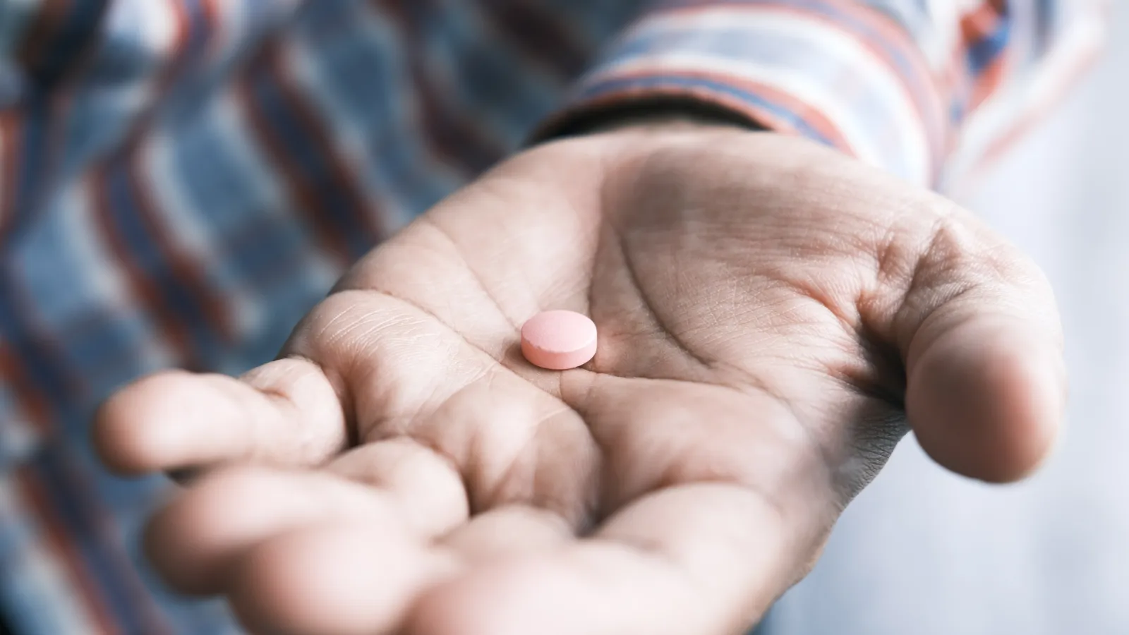 A photo of a Black man's hand holding a pill