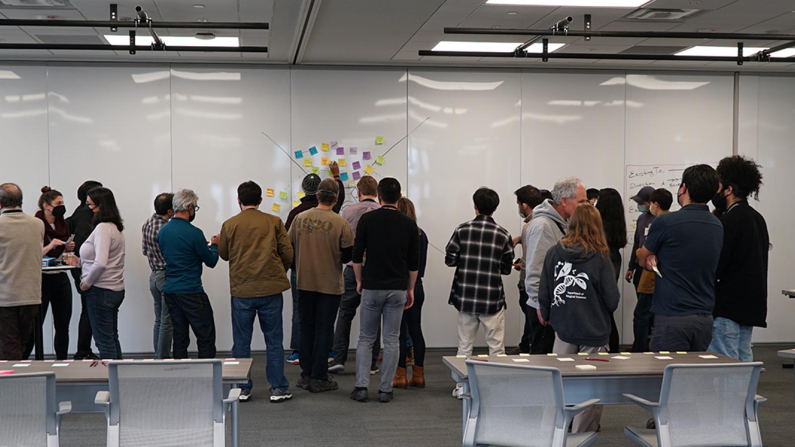 researchers standing in front of a whiteboard creating a diagram with markers and sticky notes