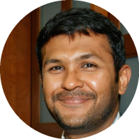 Headshot of Arnab Nandi wearing glasses and a collared shirt with a jacket, smiling against an indoor background.