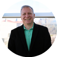 Headshot of Grzegorz Rempała smiling, wearing a light green polo and dark jacket, standing indoors with a blurred background.