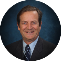 Headshot of David Noever wearing a suit and tie, smiling against a blue studio background.
