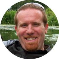 Headshot of Matthew Sullivan wearing a collared shirt, smiling outdoors with blurred greenery in the background.