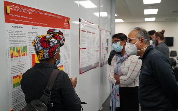 A woman explains her research poster to two men at the Fall Forum poster session