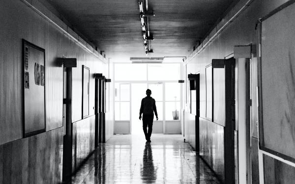 A black and white photo showing the silhouette of someone walking down a school hallways 