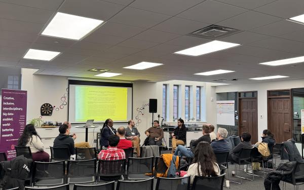 Audience members seated in a semi-circle listen to a panel discussion on human–AI systems in a collaborative event space at Ohio State.