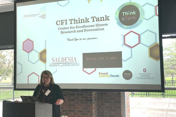 Dr. Barb Kowalcyk speaking at a podium in front of a slide show presentation