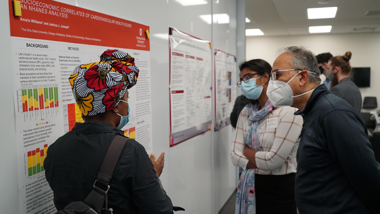 A woman explains her research poster to two men at the Fall Forum poster session 