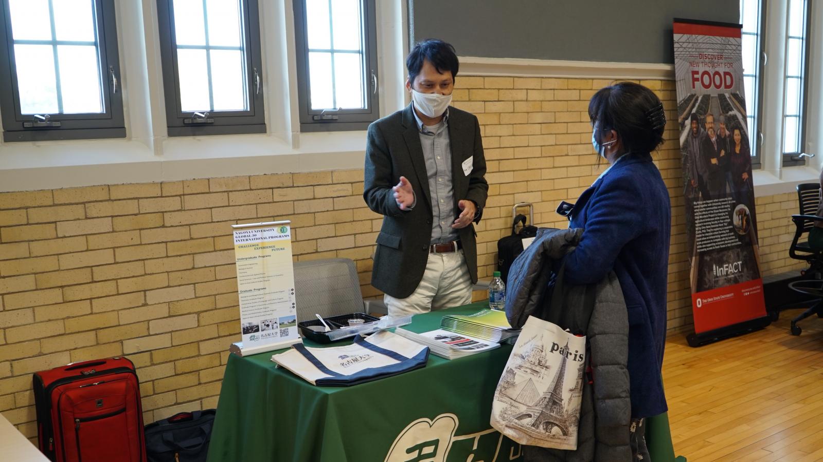 A woman and man talk at a table displaying information about Nagoya University