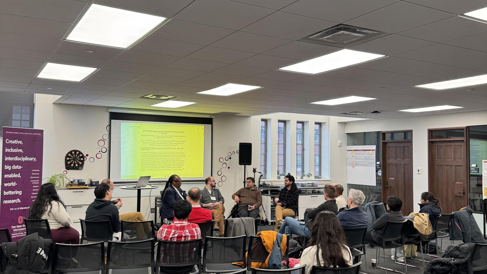 Audience members seated in a semi-circle listen to a panel discussion on human–AI systems in a collaborative event space at Ohio State.