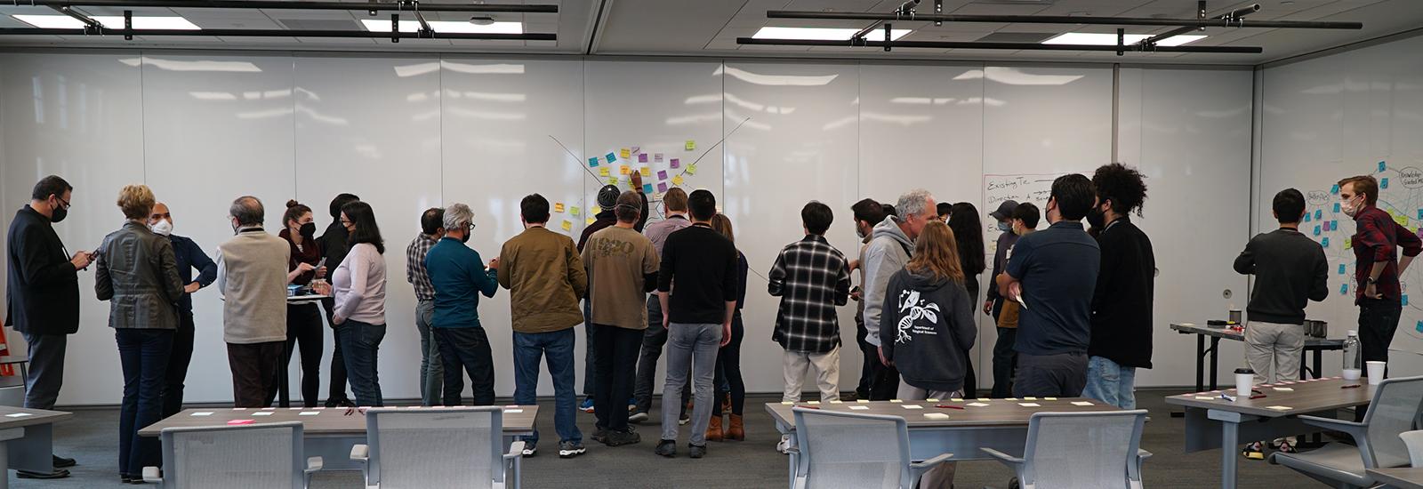 researchers standing in front of a whiteboard creating a diagram with markers and sticky notes