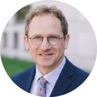 Headshot of Dennis Hirsch wearing glasses and a suit with a patterned tie, photographed outdoors.