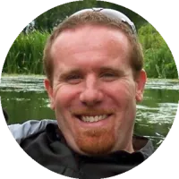 Headshot of Matthew Sullivan wearing a collared shirt, smiling outdoors with blurred greenery in the background.